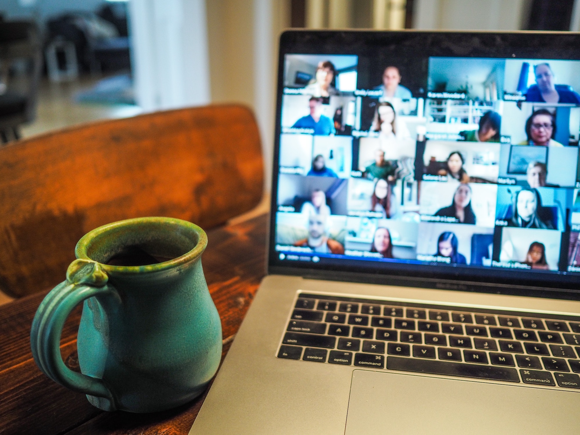 Laptop zeigt verschiedene Menschen in einer Videokonferenz, daneben steht eine Tasse