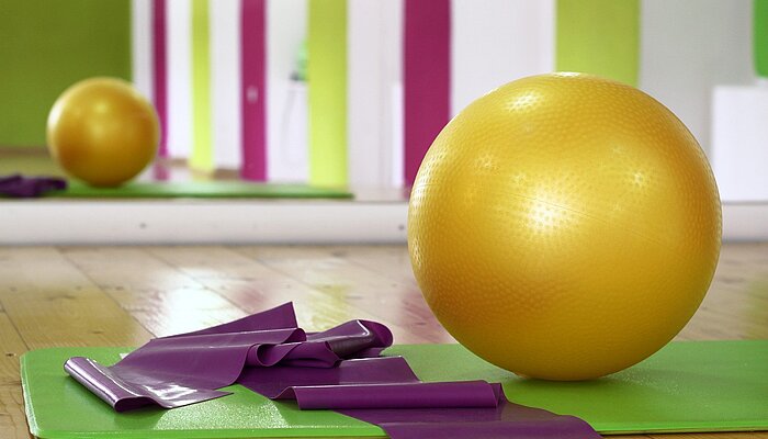 Gymnastikmatte, Gymnastikband und Gymnastikball auf dem Boden einer Turnhalle liegend