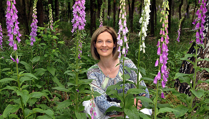 Frau hockt in einem Beet umringt von Blumen