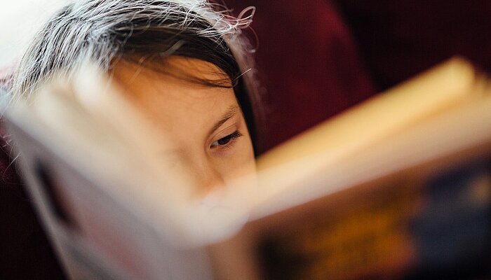 Unsplash/johnnymcclung Mädchen liest konzentriert in einem Buch.