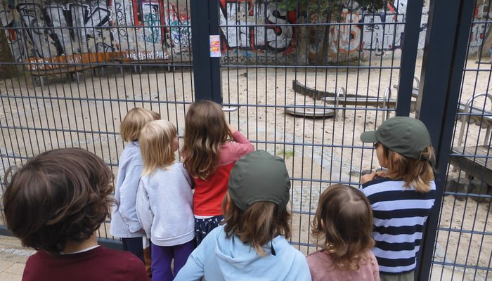 Sieben Kinder stehen vor dem Zaun eines Spielplatzes