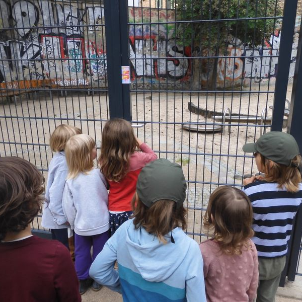 Sieben Kinder stehen vor dem Zaun eines Spielplatzes