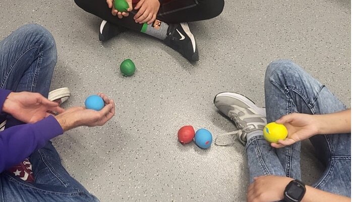 Jungen sitzen im Schneidersitz und halten bunte Bälle in den Händen