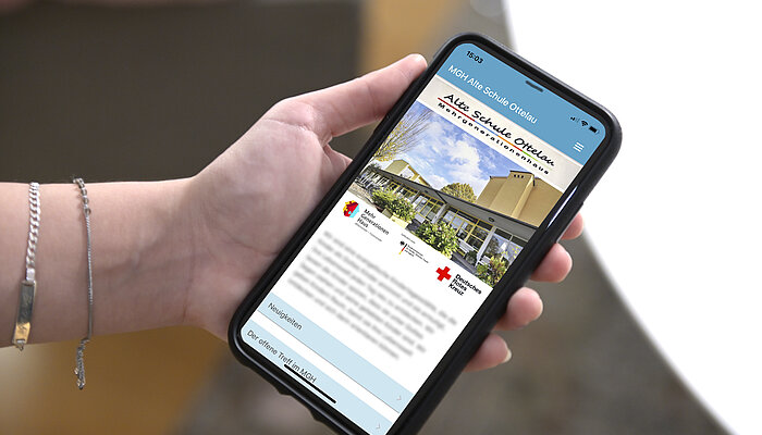 Hand hält ein Handy, auf dem die App des Mehrgenerationenhauses Alte Schule Ottelau zu sehen ist