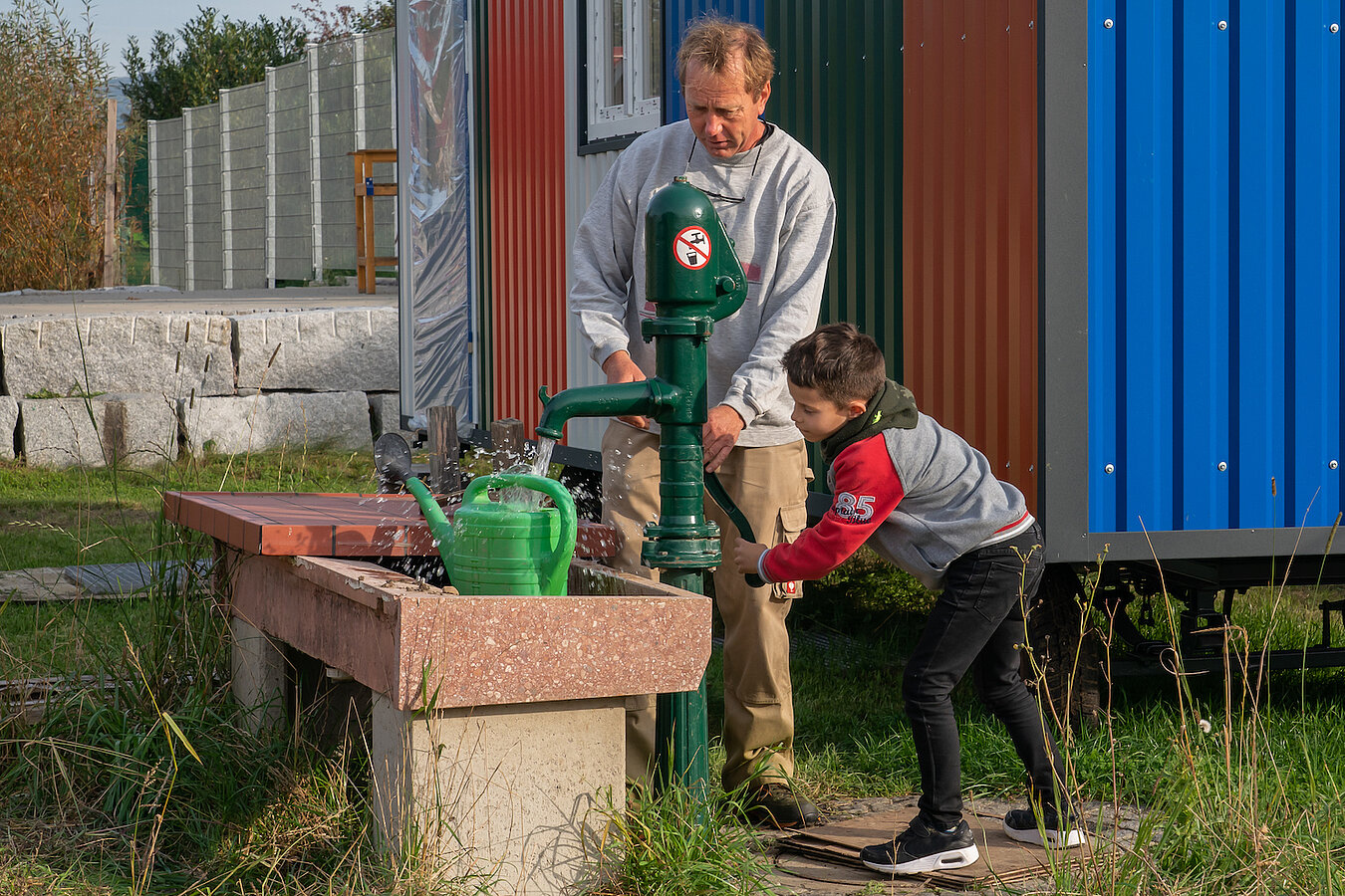 Ein Mann und ein Junge pumpen Wasser aus einem Brunnen in eine Gießkanne