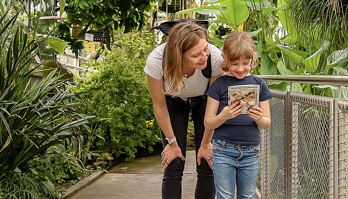 Ein Kind und eine Frau stehen zusammen in einem großen Tropenhaus eines Botanischen Gartens.