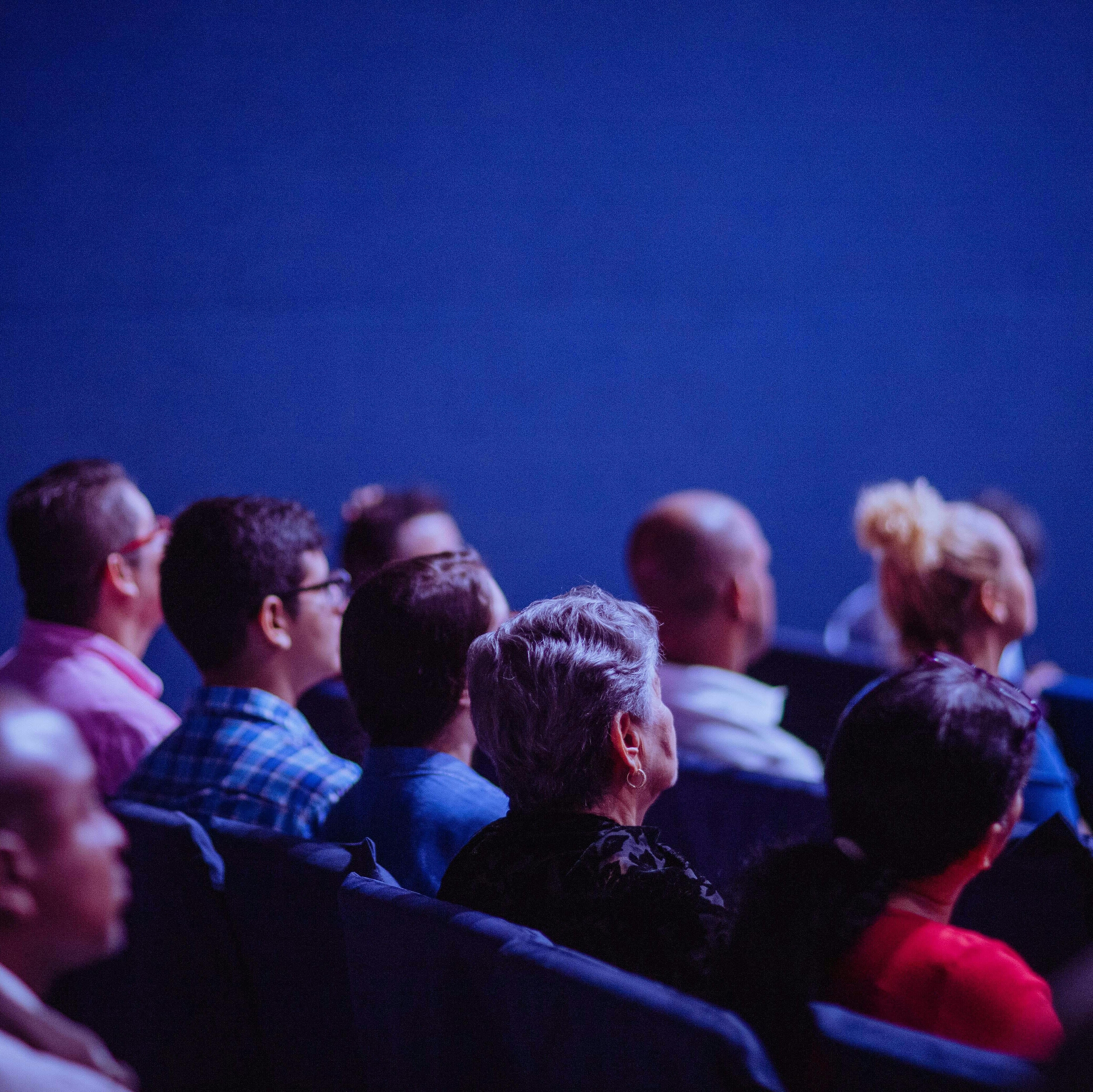 Menschen verschiedner Generationen sitzen in einem Kinosaal und schauen auf die Leinwand. 