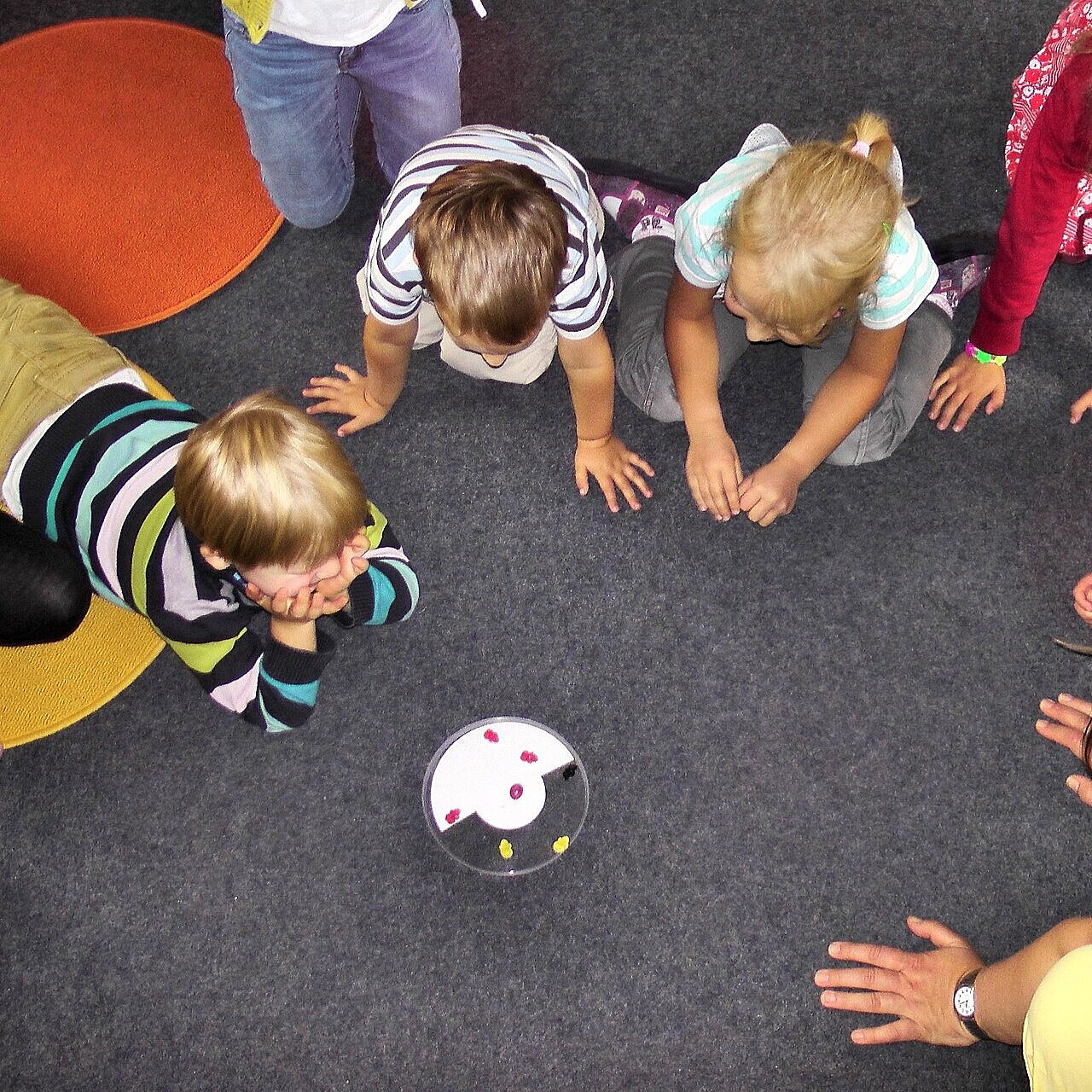 Acht Kinder und eine Frau hocken im Kreis auf dem Boden, in der Mitte steht eine Schale mit Fruchtgummi