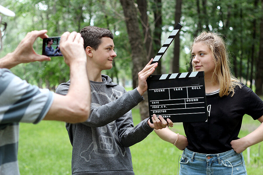 Zwei Jugendliche werden von einem Smartphone gefilmt, einer von ihnen hält eine Filmklappe in der Hand.
