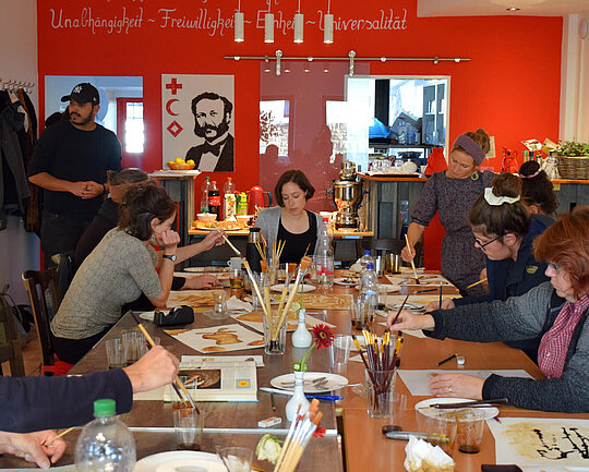 Mehrere Personen sitzen an einem großen Tisch und malen mit Wasserfarbe