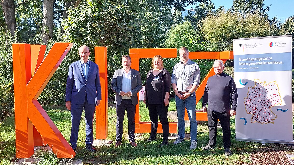 Vor dem Wort "Kiez" stehen (von links nach rechts): Michael Brand (Parlamentarischer Staatssekretär), Martin Schaefer (Bezirksbürgermeister Lichtenberg), Anne Stöckmann (stellv. Geschäftsführerin Kiezspinne, Koordinatorin MGH), Christian Gridel (Geschäftsführer Kiezspinne), Andreas Svojanovsky (1. Vorsitzender des Vorstands Kiezspinne)