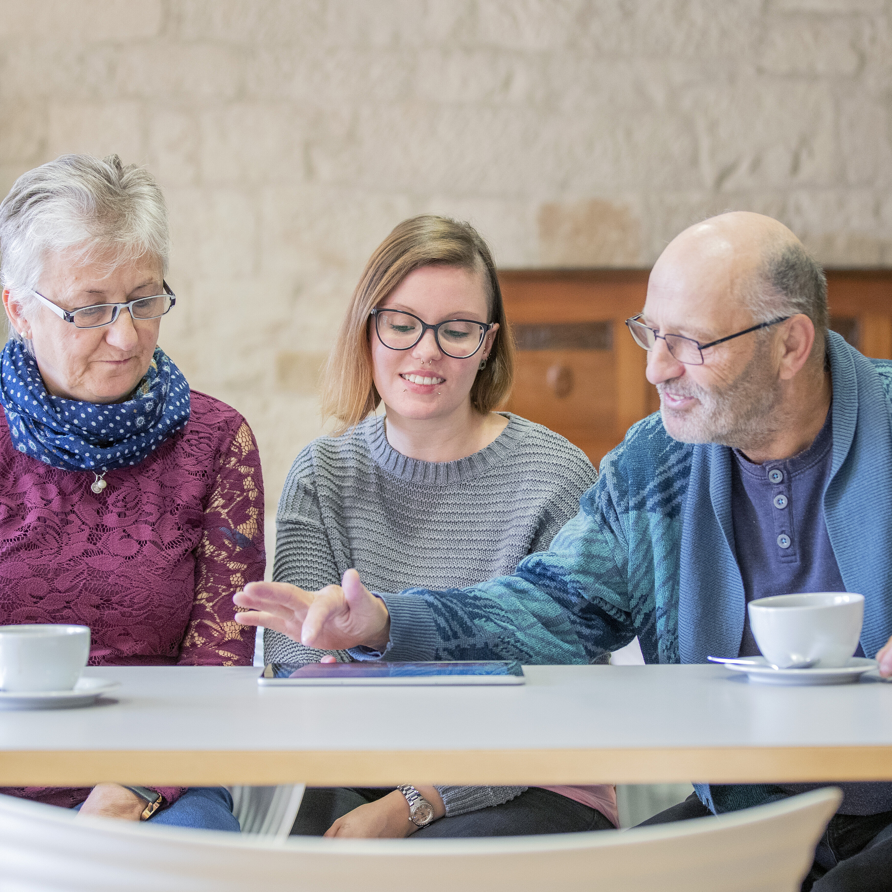 Seniorinnen und Senioren sitzen zusammen mit einer jungen Frau lächelnd an einem Tisch über ein Dokument gebeugt