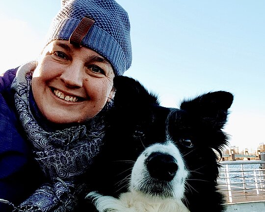 Christina Meyer lacht in die Kamera, neben ihr sitzt ihr Hund Curly 