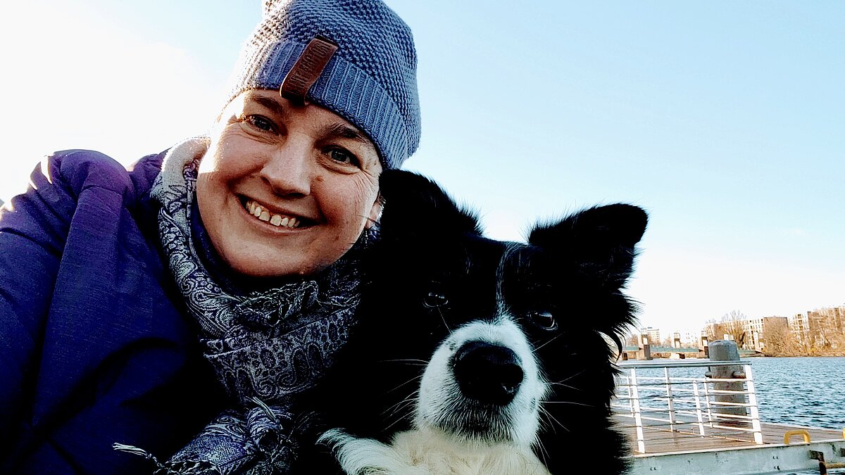 Christina Meyer lacht in die Kamera, neben ihr sitzt ihr Hund Curly