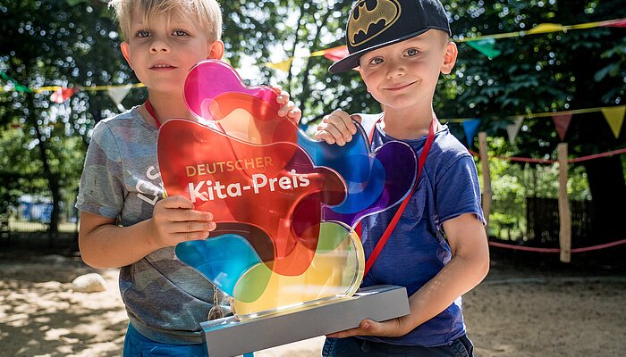 Zwei Kinder halten die Trophäe des Deutschen Kita-Preises stolz in die Kamera