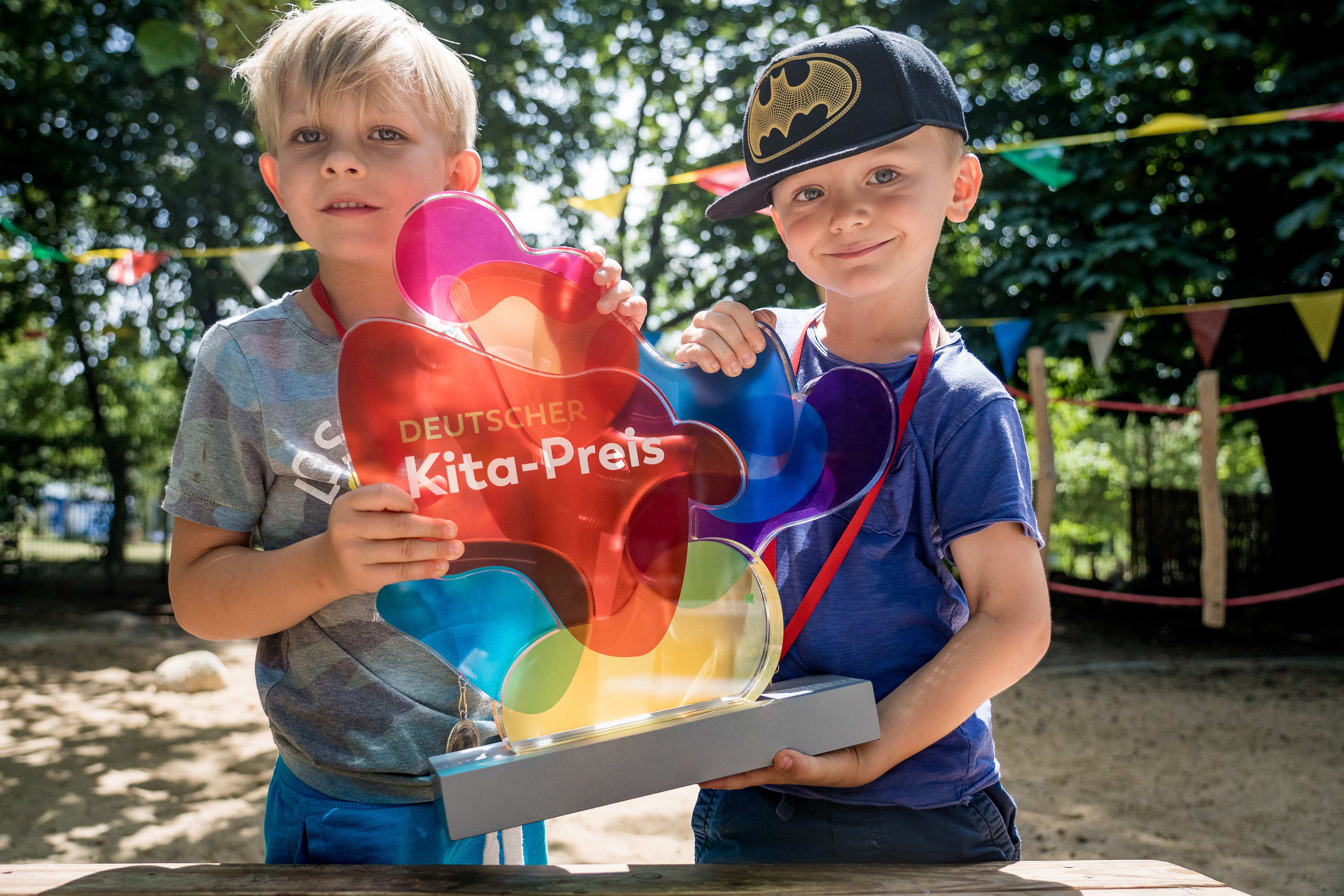 Zwei Kinder halten die Trophäe des Deutschen Kita-Preises stolz in die Kamera